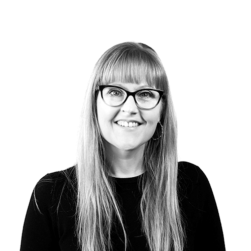 A Black and White of staff member Rebekah. She has long hair, glasses, and is smiling.