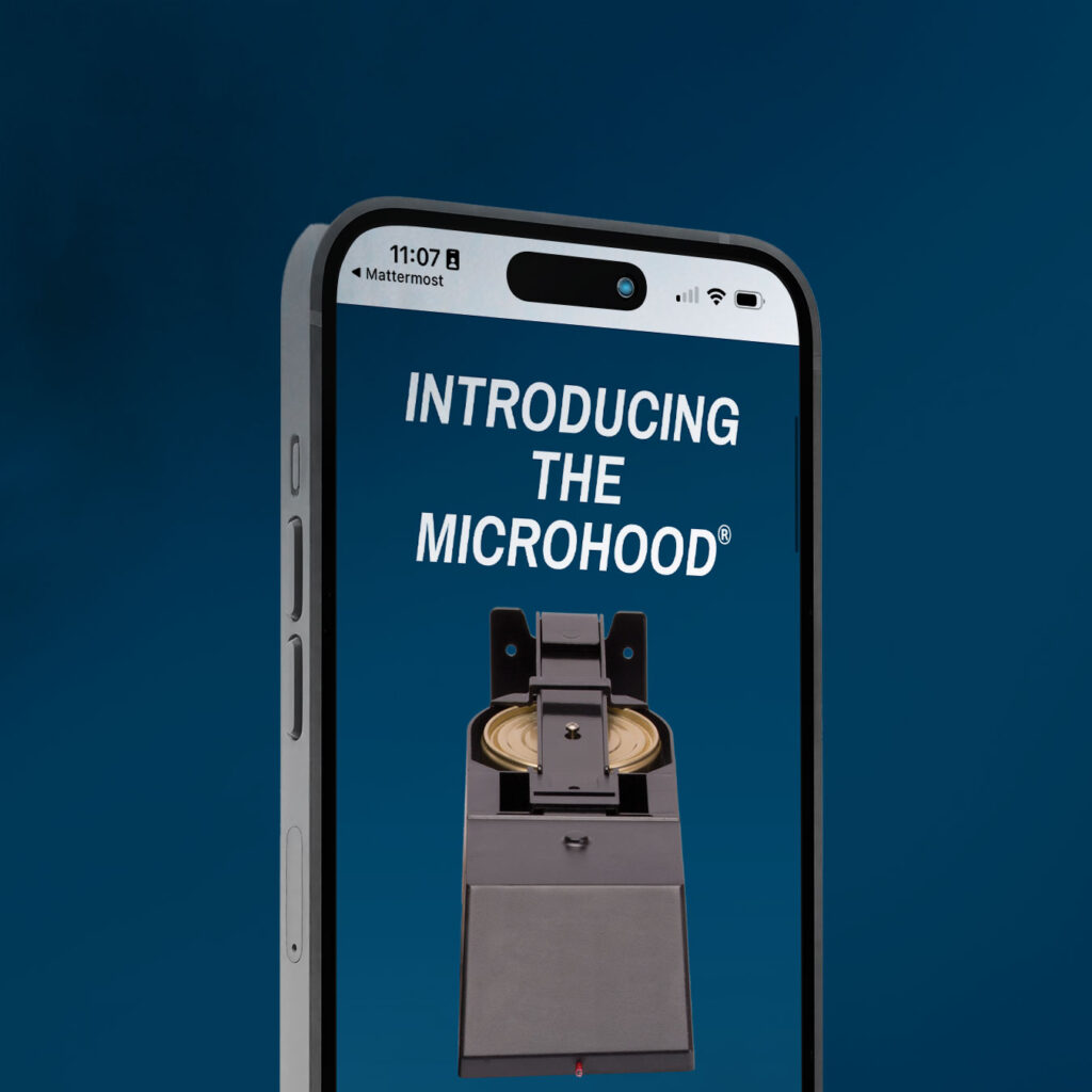 A smartphone screen displays an ad for "The Microhood," a small appliance with automatic fire suppression, shown with an open door and a plate inside against a blue background.