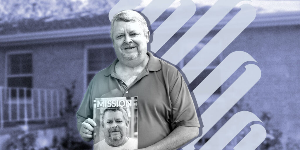 A man stands in front of a building, holding a magazine with his photo on the cover, showcasing his achievements in web design.