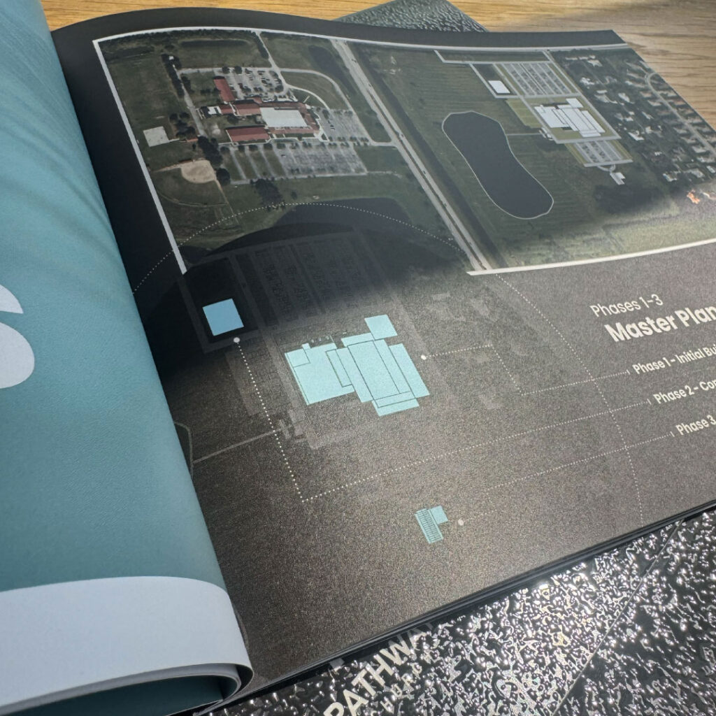 A close-up of an open book displaying an aerial site plan with labeled areas and a “Master Plan” heading on the right page, showcasing print design work for Goff Companies.
