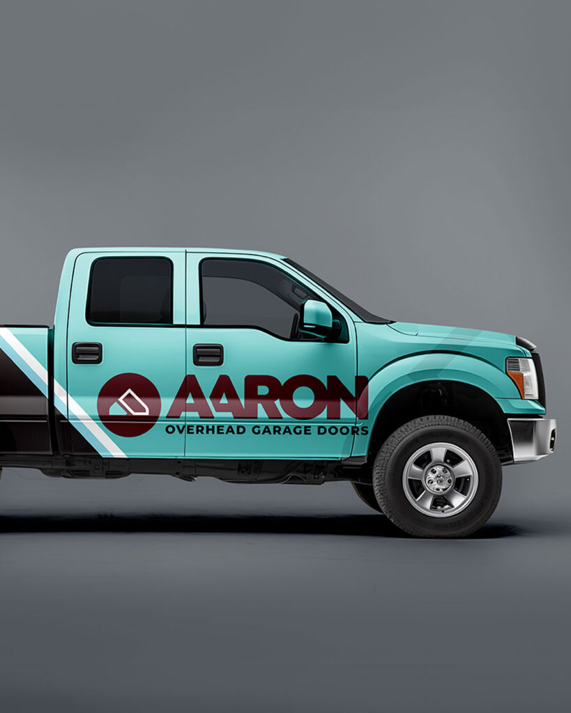 A teal and black pickup truck with the "Aaron Overhead Doors" logo and text on the side, parked against a plain gray background.