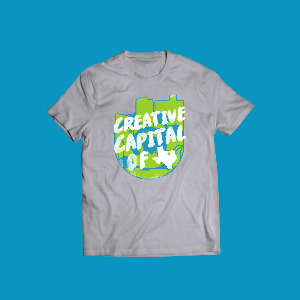Gray t-shirt with an ardent graphic design featuring a city skyline and the words "Creative Capital of" in bold white and green text on a blue background—perfect for fans of inspired logo design.