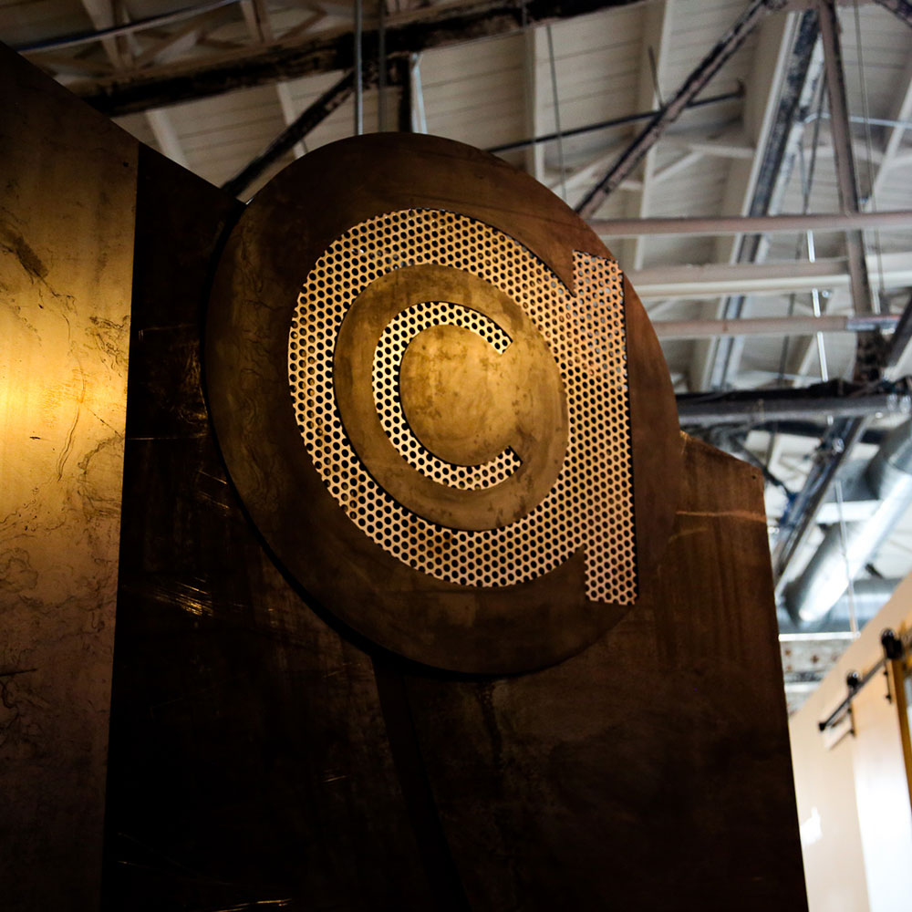 A large metallic copyright symbol sign, evoking logo design and brand evolution, is mounted on a dark wall inside a building with an exposed ceiling structure.